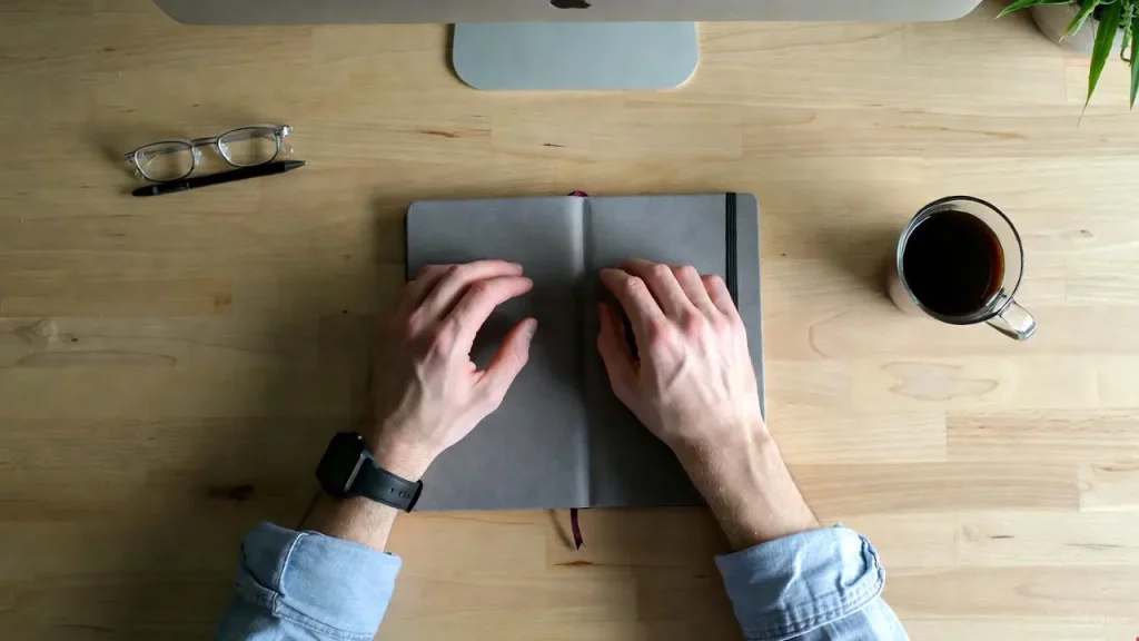 Hands resting peacefully on a clean, wooden desk after achieving a minimalist office setup.